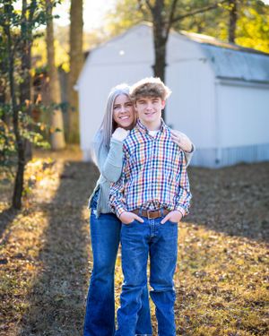 Casual portrait of two people hugging and smiling in front of a white shed on an autumn day.