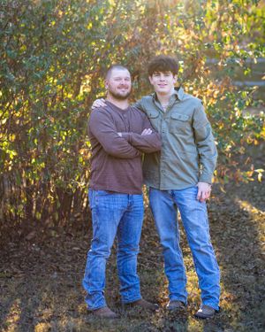 Two people in casual attire posing together against colorful fall foliage.