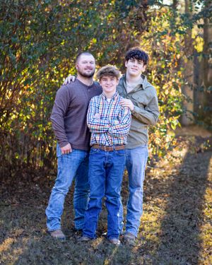 Three people standing close together for a portrait with fall foliage behind them.