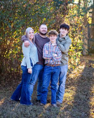 Family of four posing together outdoors with autumn trees and golden light in the background.