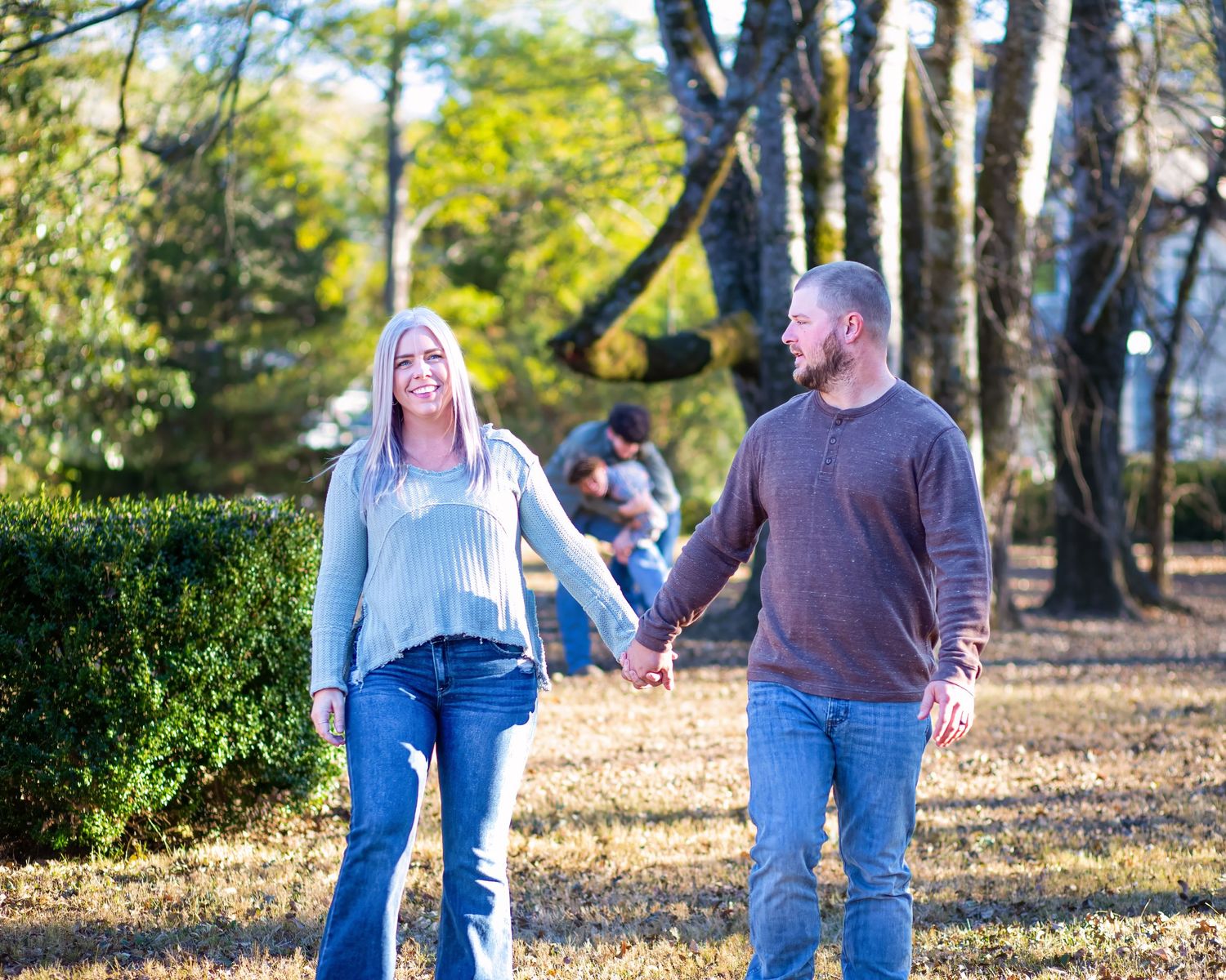 Couple walking hand in hand along a tree-lined path on a sunny autumn day.