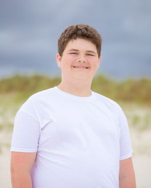 Portrait of person in white t-shirt on beach with cloudy sky backdrop.