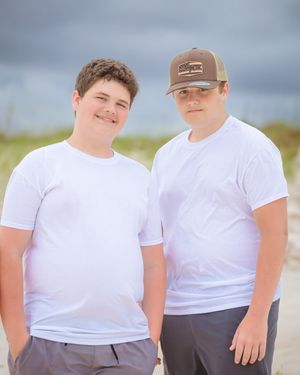 Two people in white t-shirts pose for photo on beach with cloudy sky.