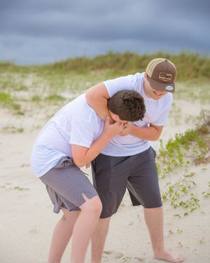 Two people in white shirts playfully interact on sandy beach dunes.