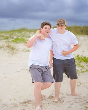 Two people in casual beach attire pose playfully on sandy dunes.