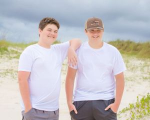 Two people in white t-shirts share casual moment on beach with dunes.