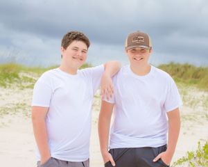 Two people in white shirts pose casually against beach dunes background.