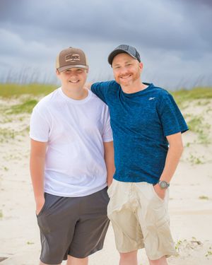 Two people standing together on beach dunes wearing casual attire on an overcast day.