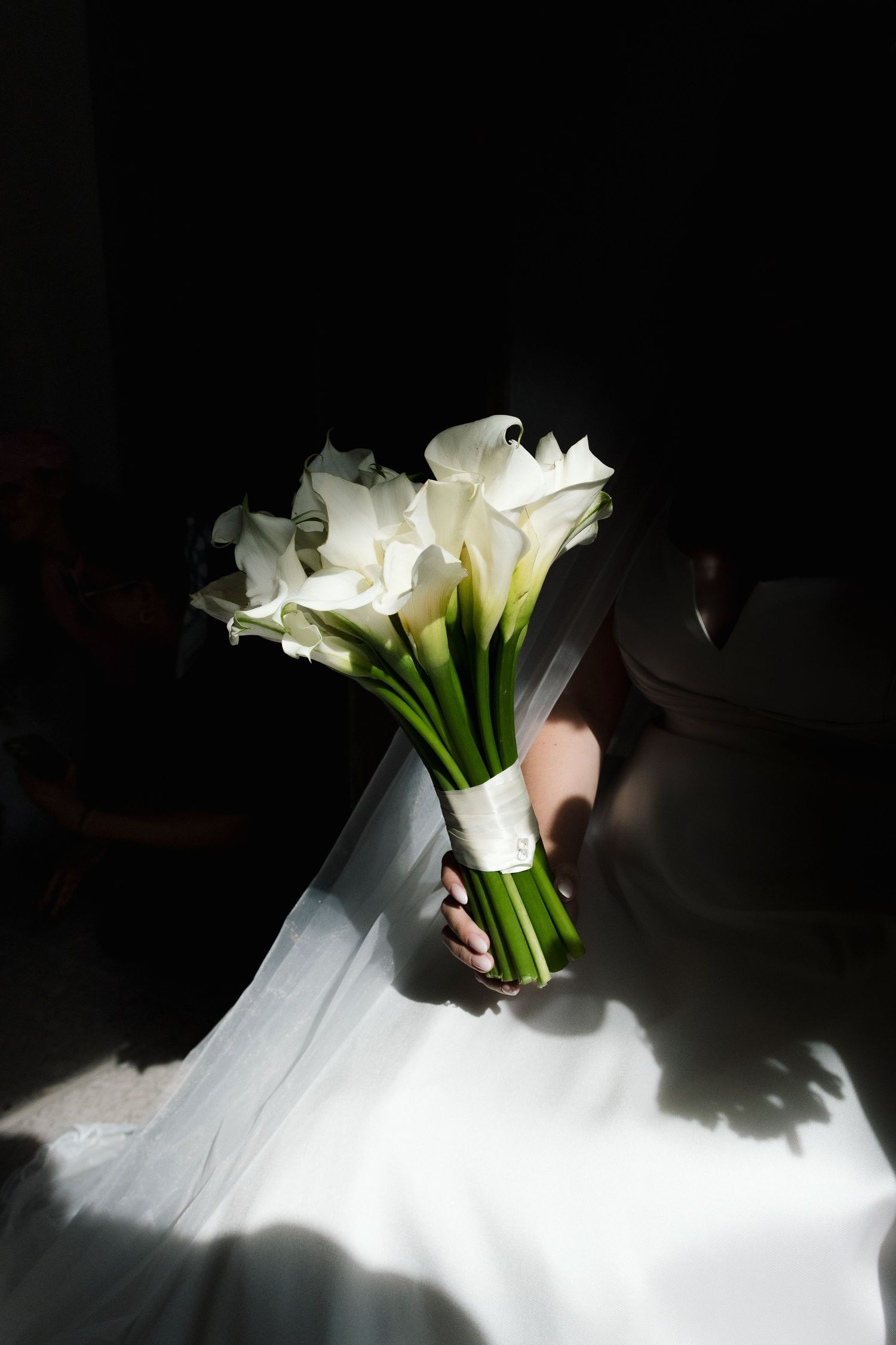Dramatic lighting on white calla lily bouquet against dark background.