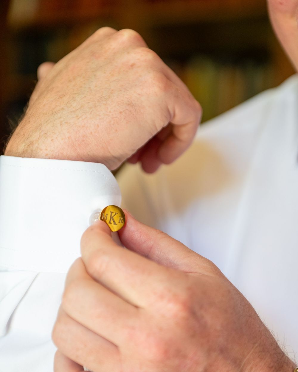 Man fastening a gold monogram K cufflink on a white dress shirt sleeve.