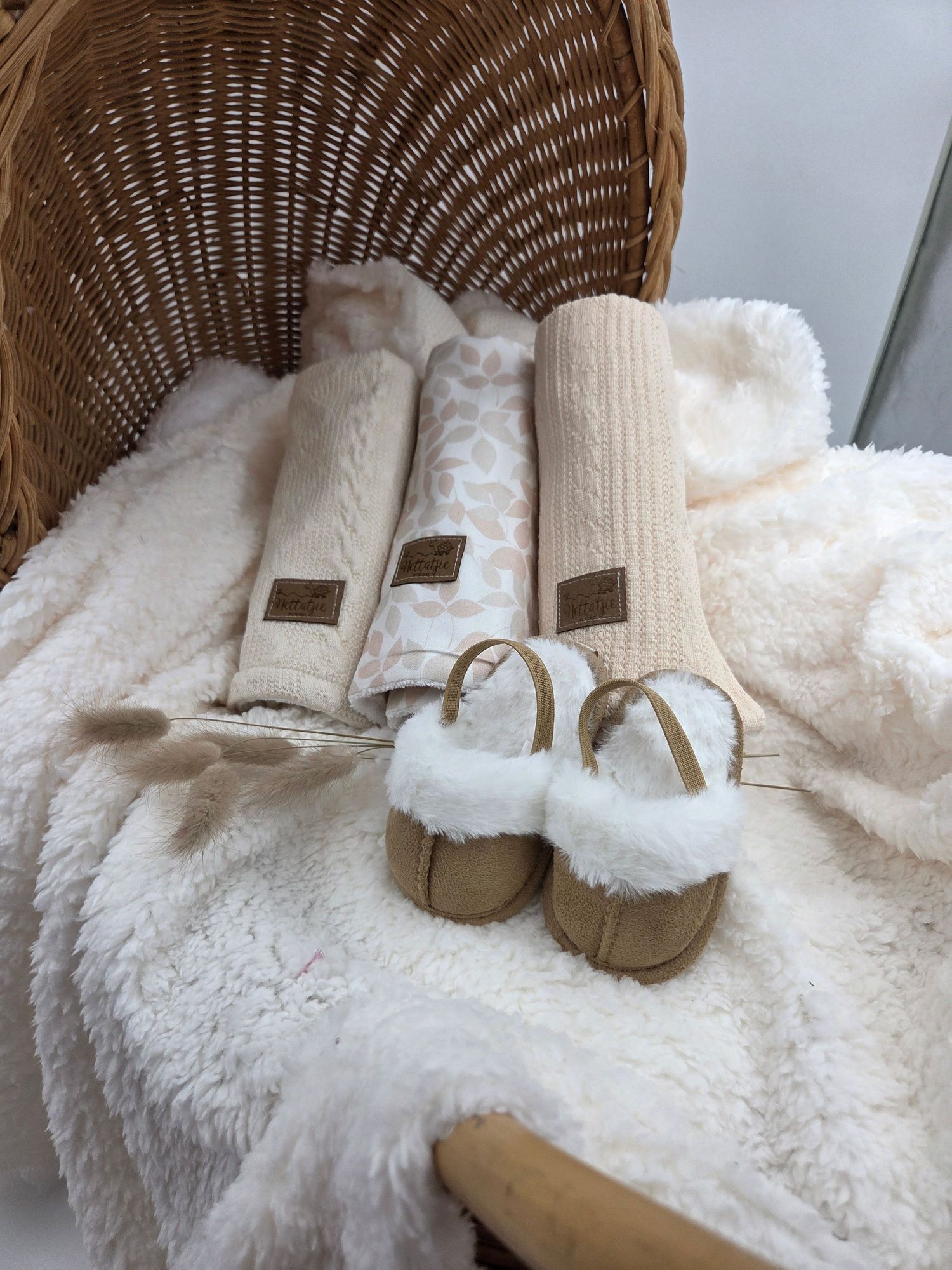 White fuzzy blankets and fur-lined sandals arranged in wicker chair.