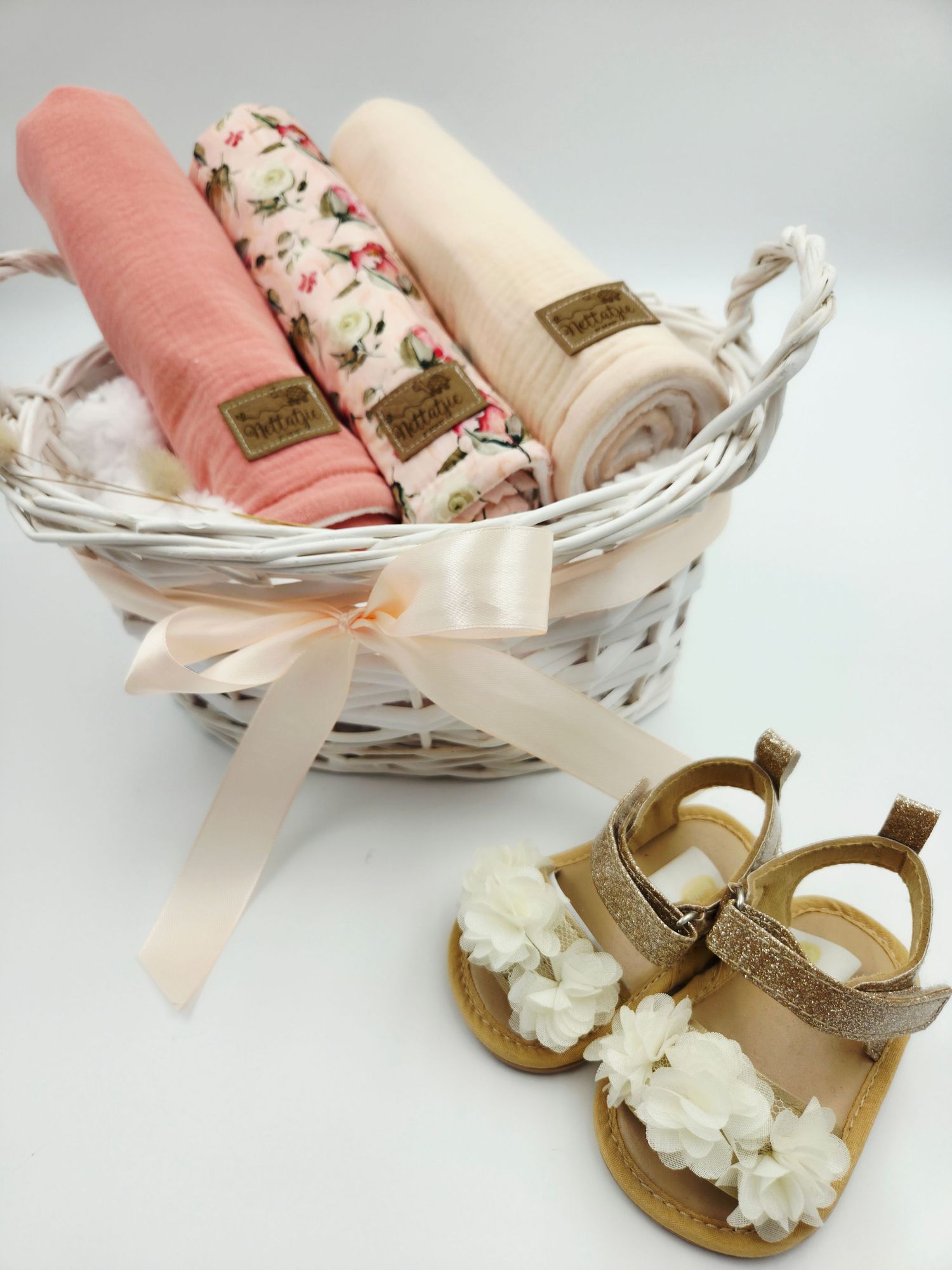 Pink and floral baby blankets in white basket with decorative sandals.