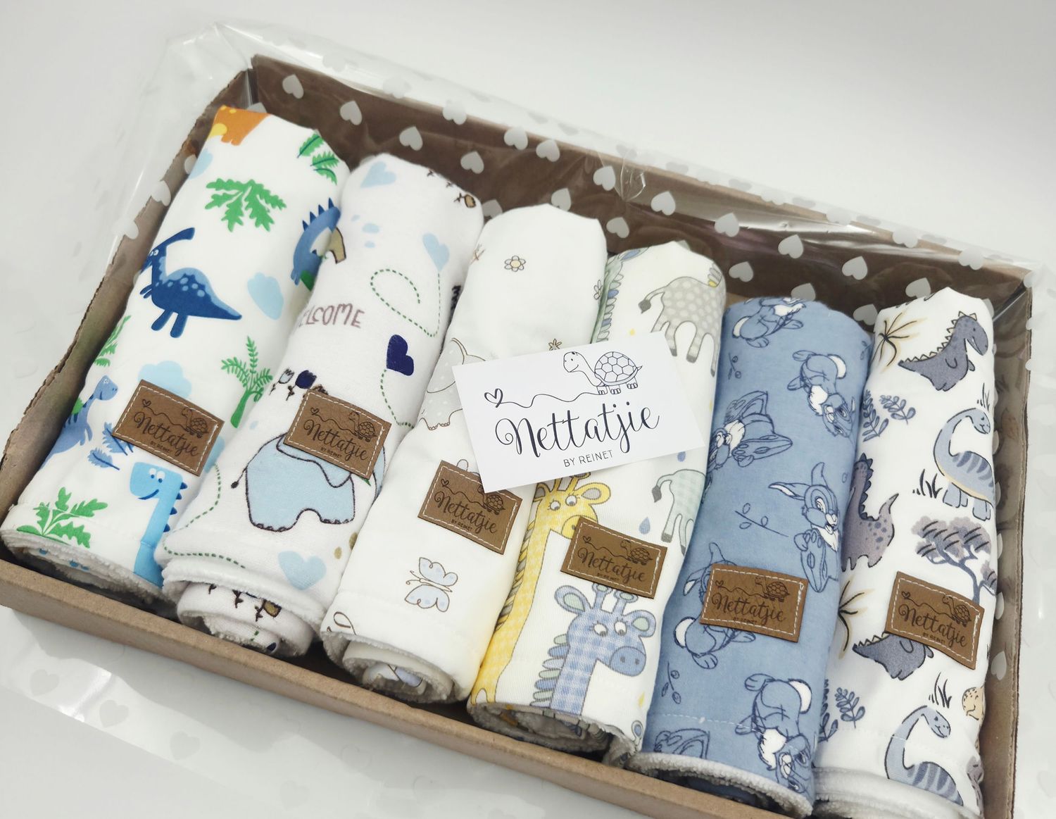 Collection of baby blankets with elephant and dinosaur prints arranged in a wooden box display.