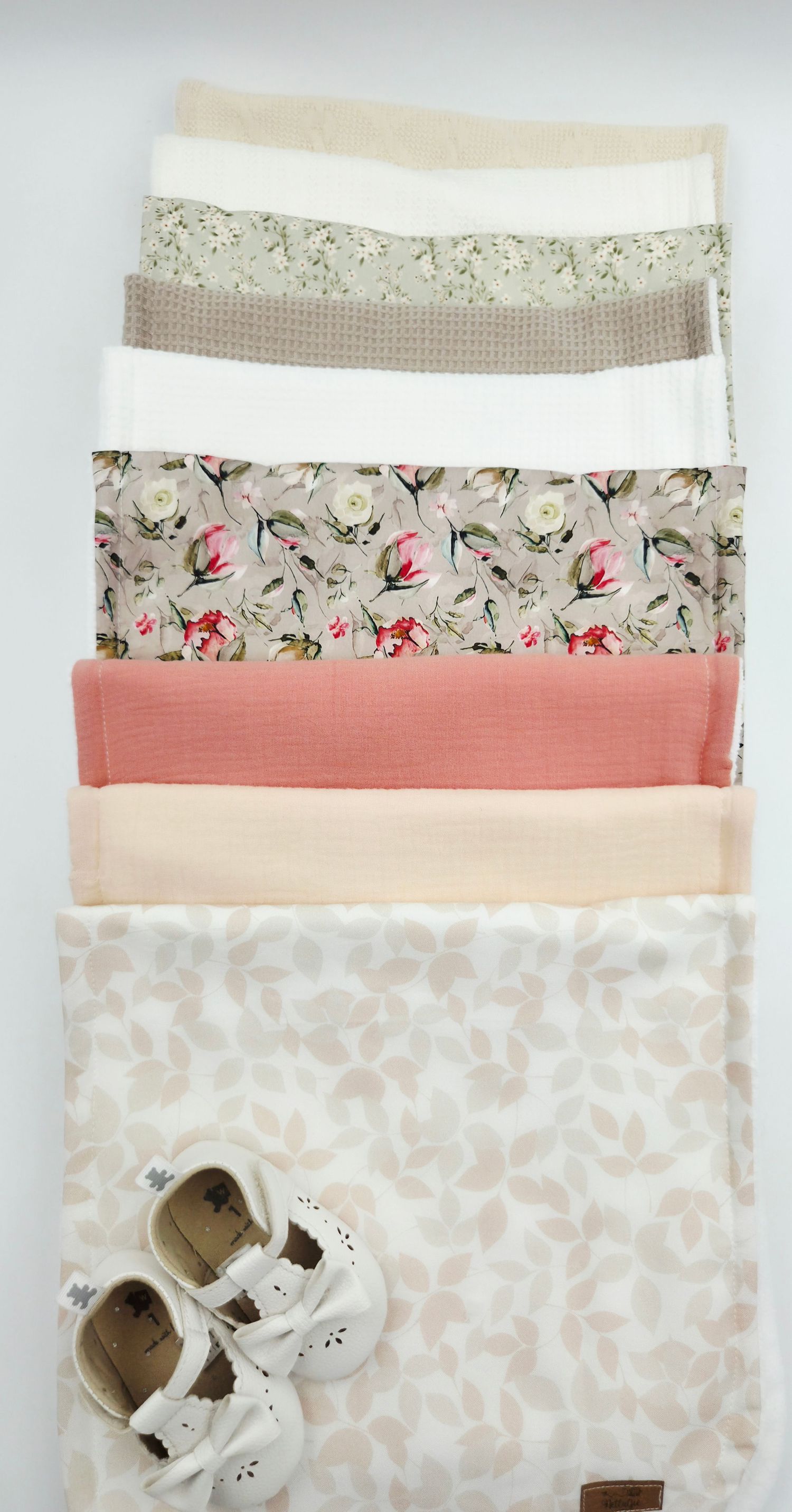 Neutral toned baby blankets with floral patterns and soft textures stacked in coordinating layers.
