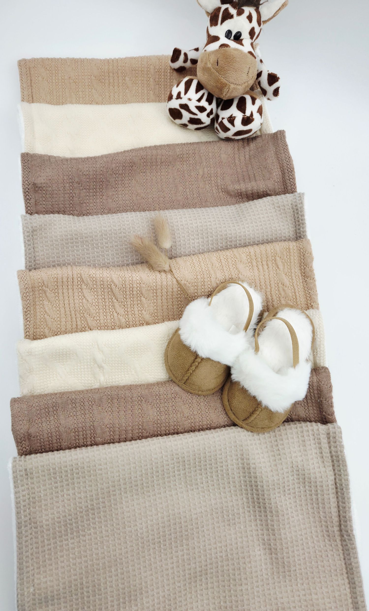Beige and cream textured baby blankets with plush animal accessories arranged in layers.
