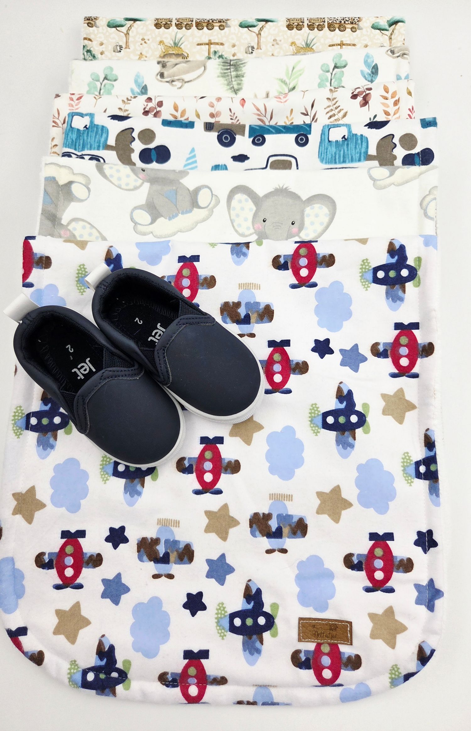 White baby blanket with airplane and star pattern displayed with navy blue baby shoes.