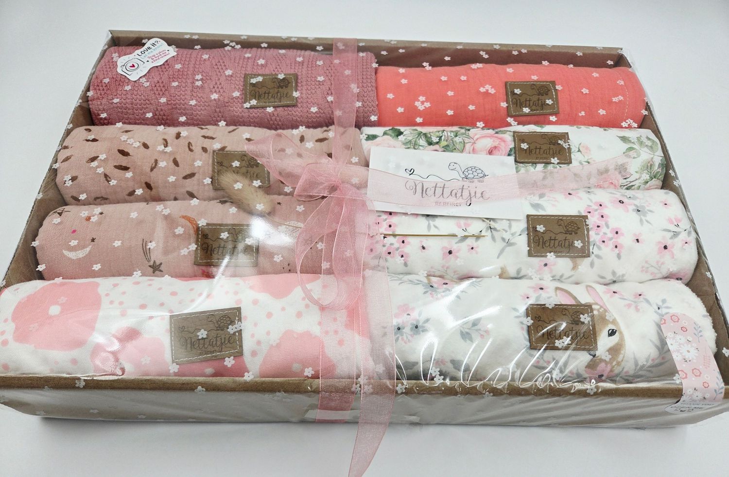 Pink and coral baby blanket gift sets with delicate patterns displayed in retail packaging.