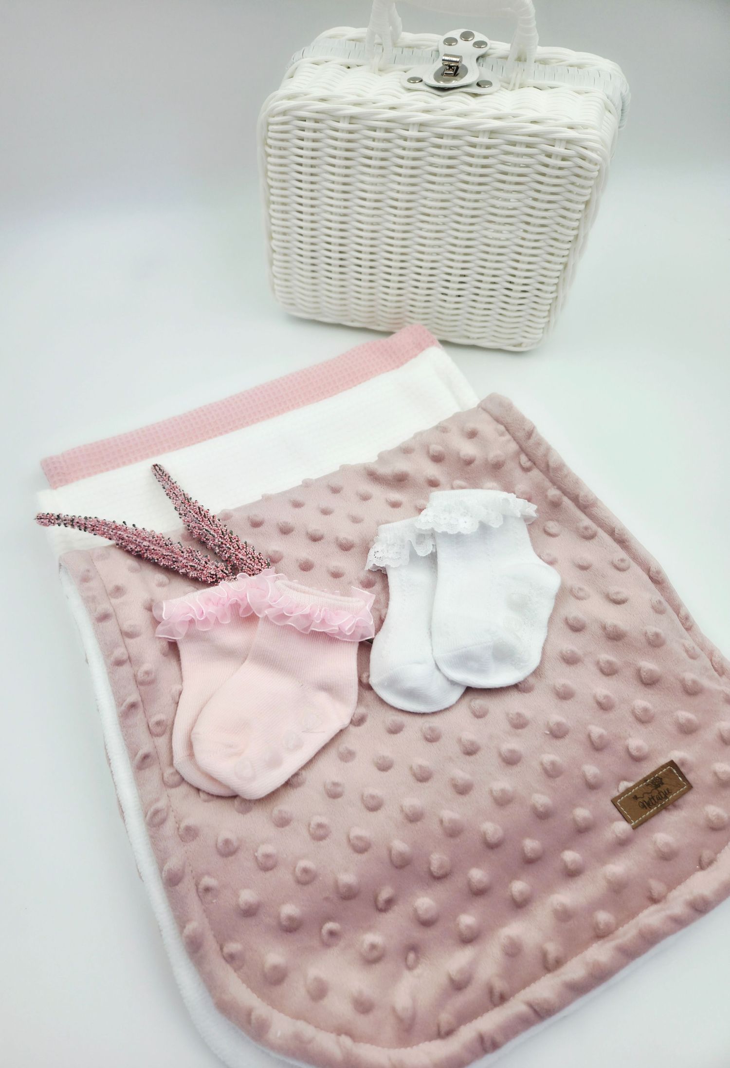 Pink minky baby blanket with white socks and hair bow displayed next to white wicker basket.