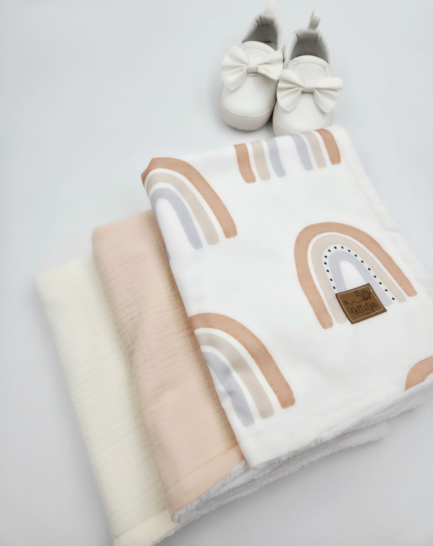 Neutral rainbow pattern baby blankets with white bow shoes and beige accents.