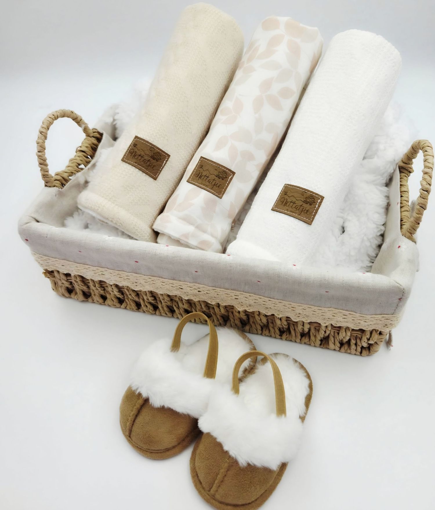 Wicker basket containing cream colored baby blankets with matching fuzzy moccasins.
