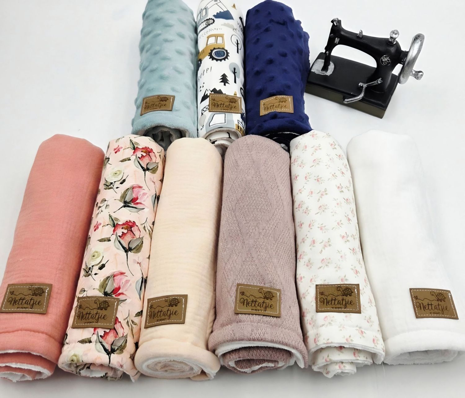 Collection of soft pastel and floral print baby swaddle blankets with leather labels arranged in a row.