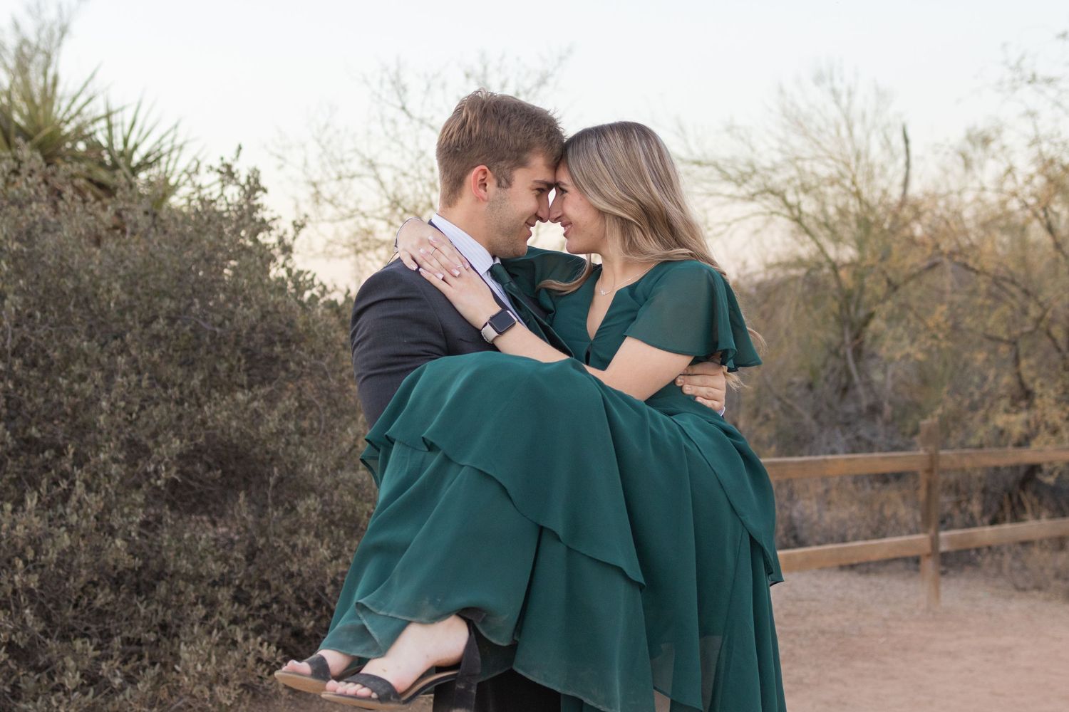 Couple shares intimate moment as Jack carries Kaylee in emerald dress during outdoor photoshoot.