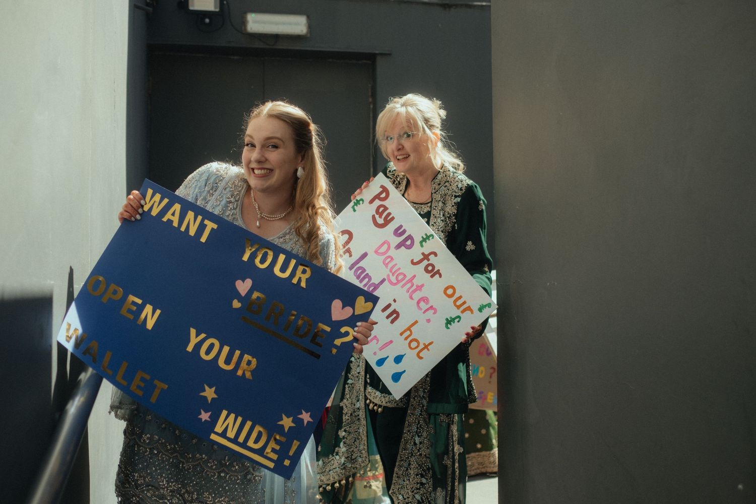 Brides family holding up wedding signs for the groom saying, Pay up for our daughter or land in hot water.