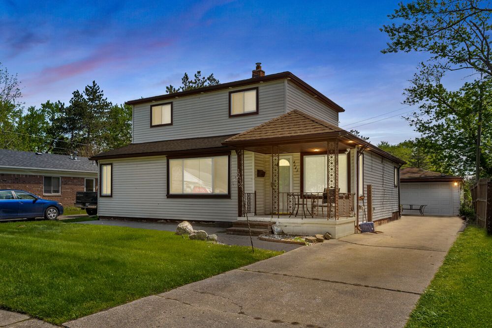 Two-story suburban home with brown roof, covered front porch, attached garage, and well-maintained lawn at dusk.