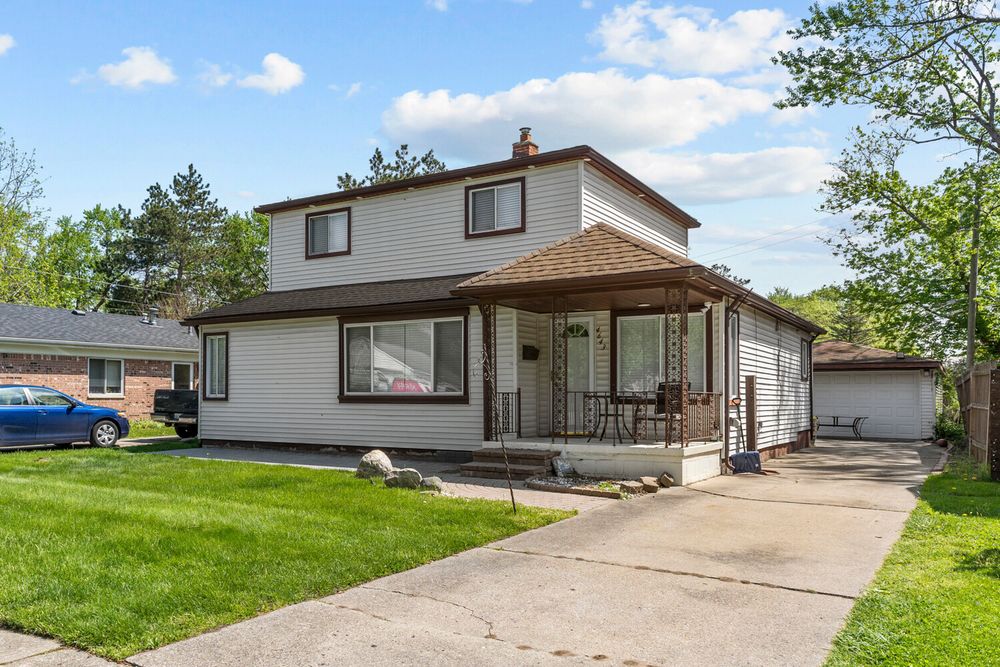 Two-story home with brown hip roof, covered front porch, manicured green lawn, and detached garage in daylight.