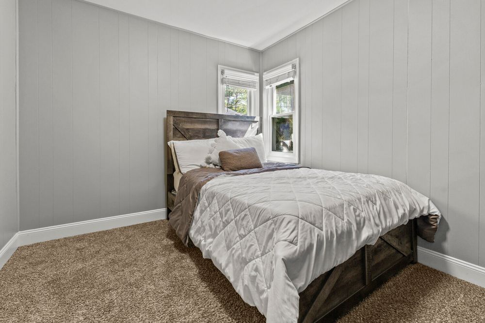 Cozy bedroom with dark wood bed frame, white bedding, and neutral carpet flooring.