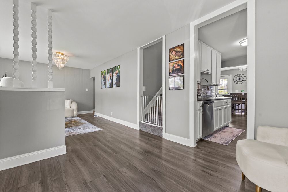 Open hallway with dark hardwood floors, staircase, and view into modern kitchen.