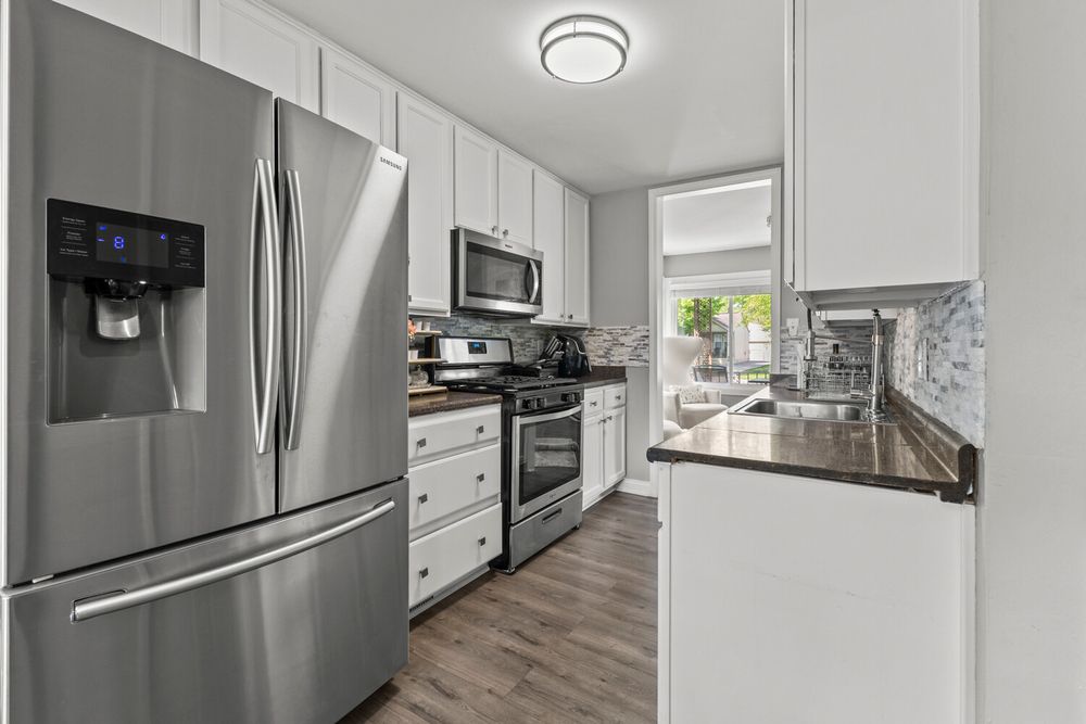 White kitchen with stainless steel refrigerator, gas range, and mosaic tile backsplash.