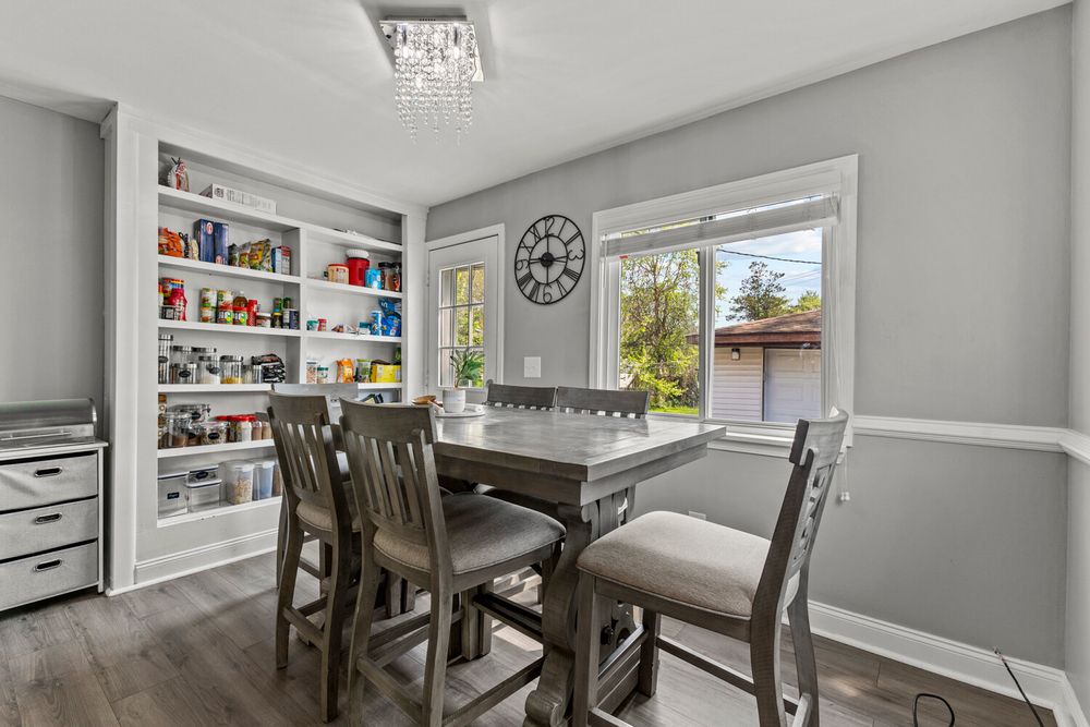 Casual dining area with built-in shelves, dark wood table, and bright window views.