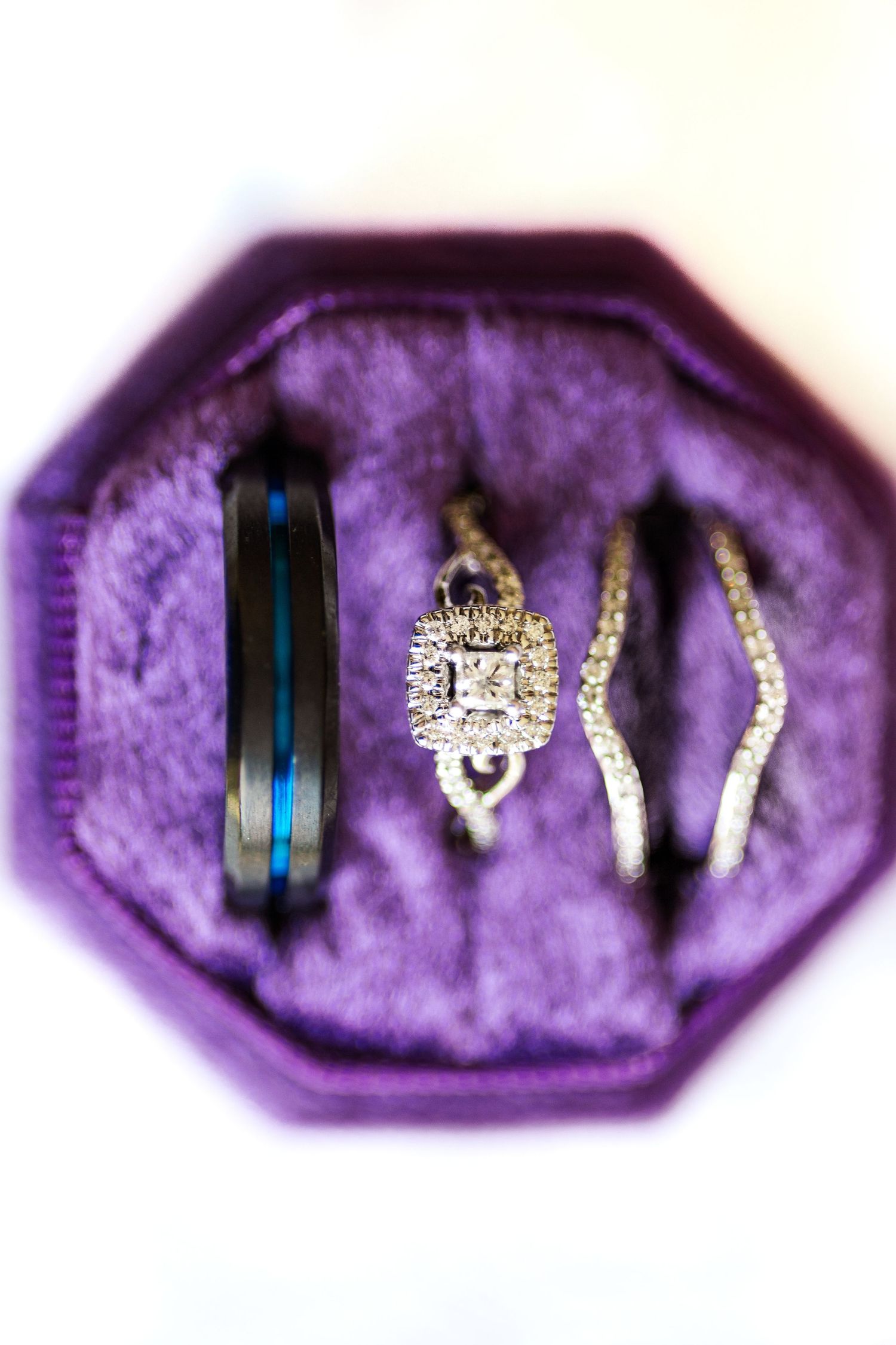 Wedding rings and engagement ring nestled in a purple velvet ring box.