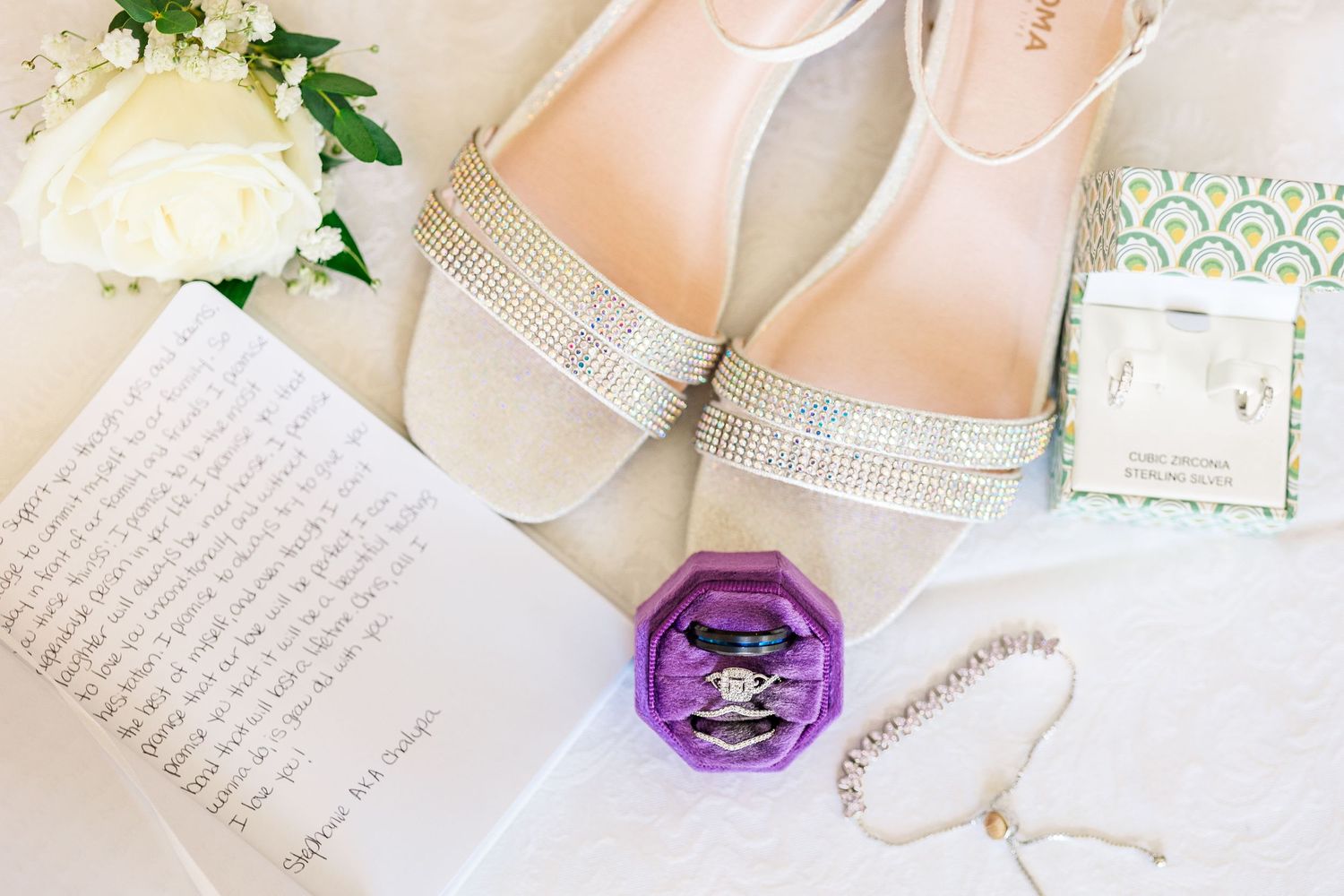 Wedding accessories including sparkly shoes, rings, and handwritten vows on white background.