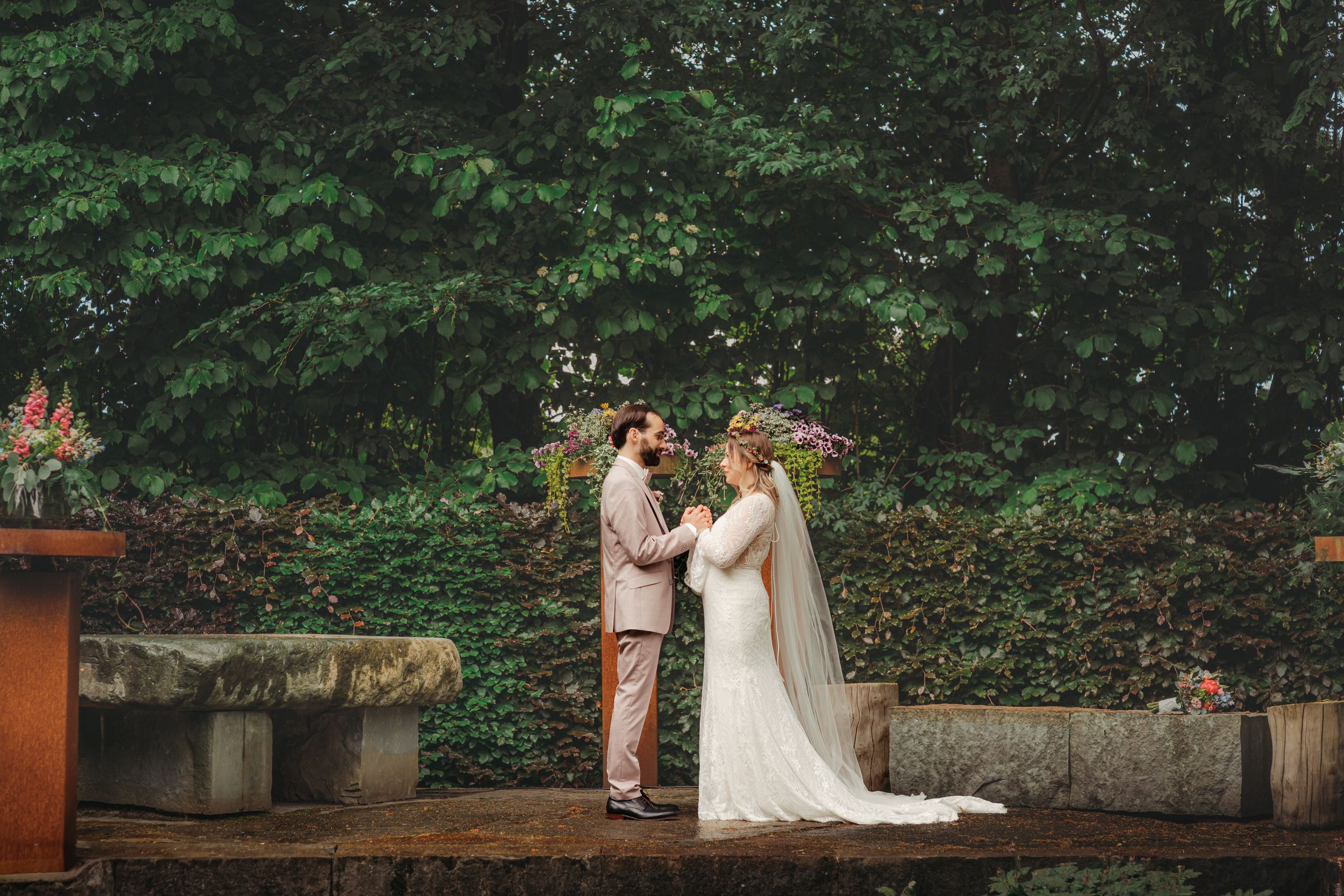 Wedding couple shares an intimate moment in a lush garden setting with stone walls and greenery in the background.