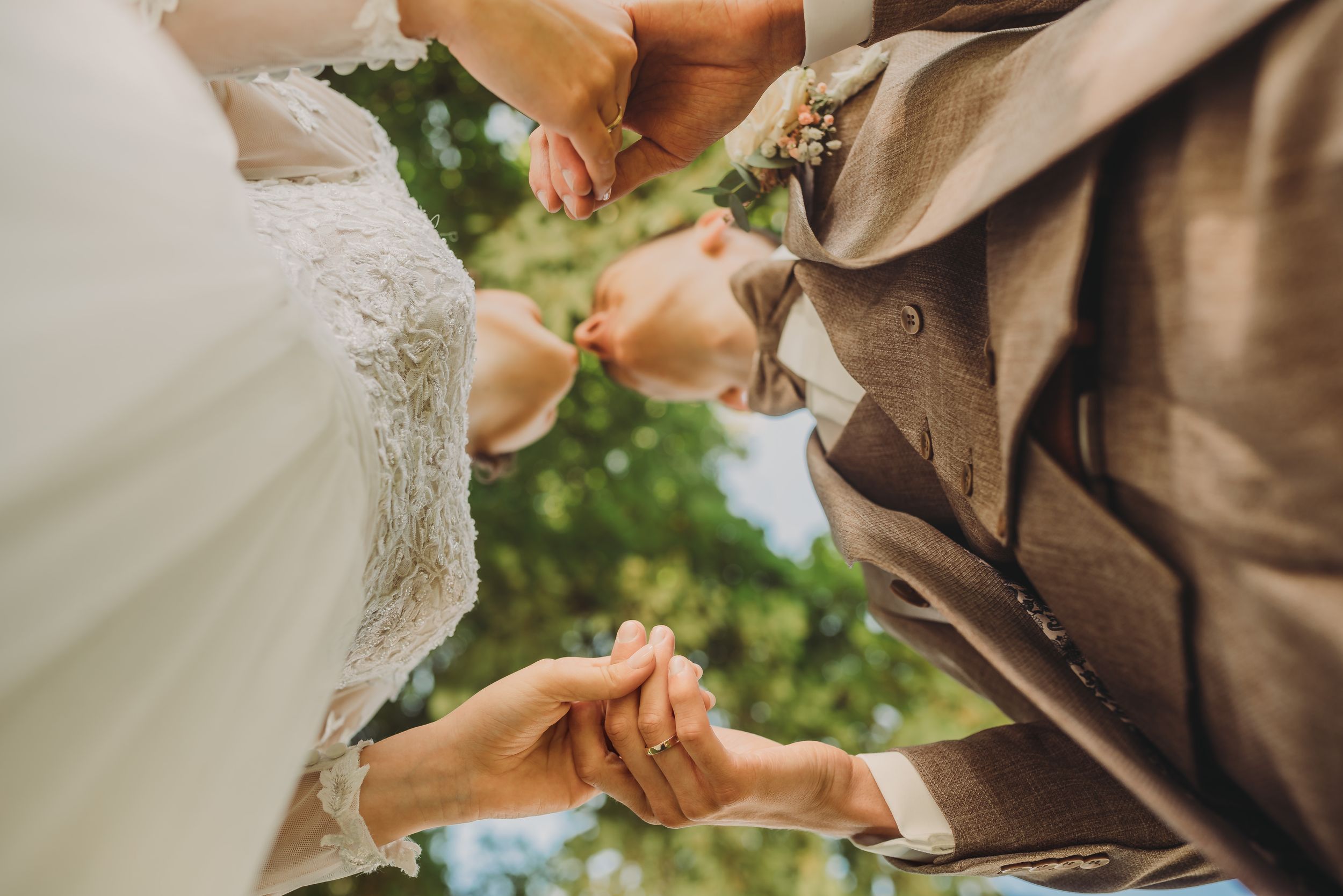 Close up view of hands exchanging wedding rings during an outdoor ceremony in natural lighting.