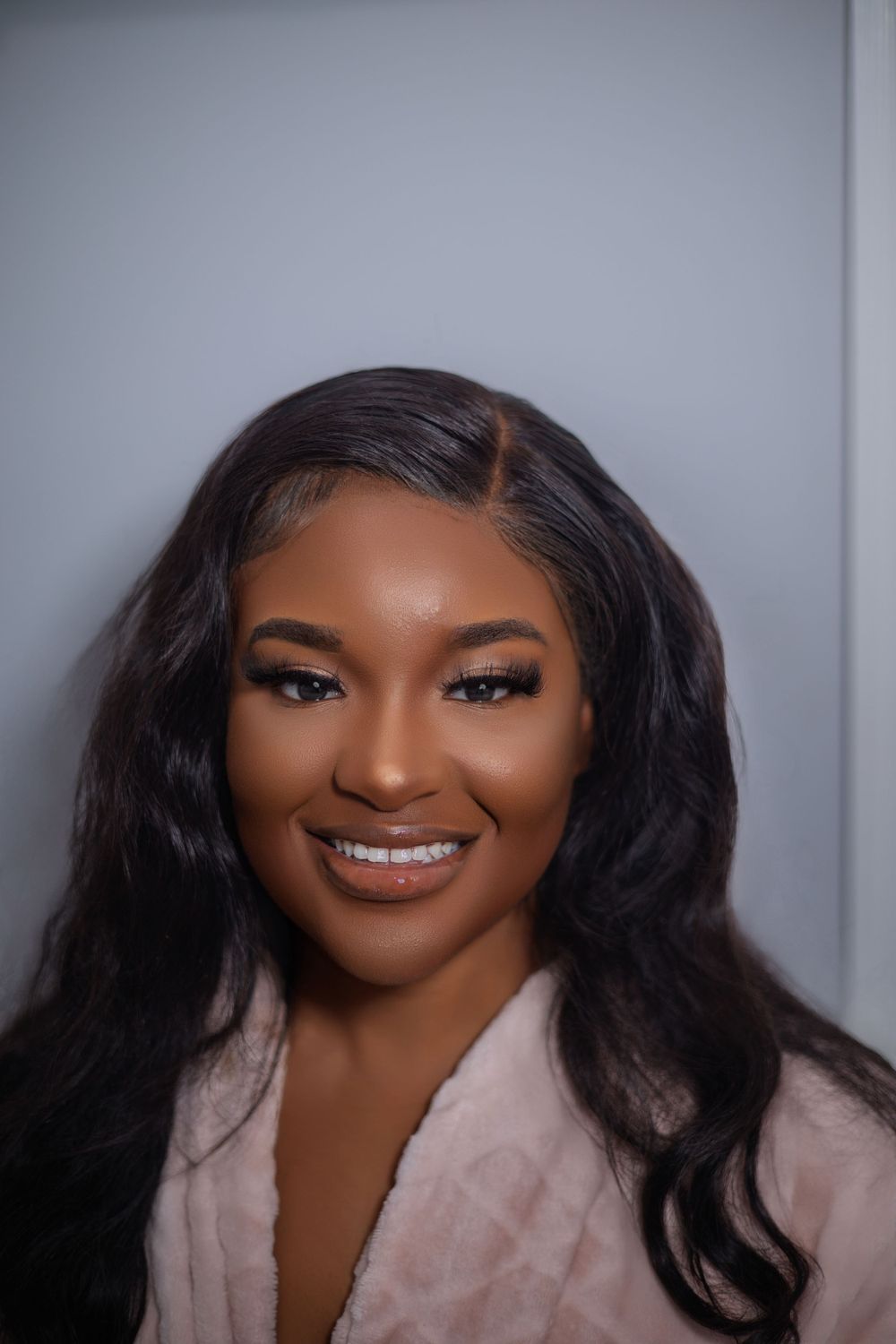 Professional headshot featuring glowing makeup and flowing hairstyle against grey background.