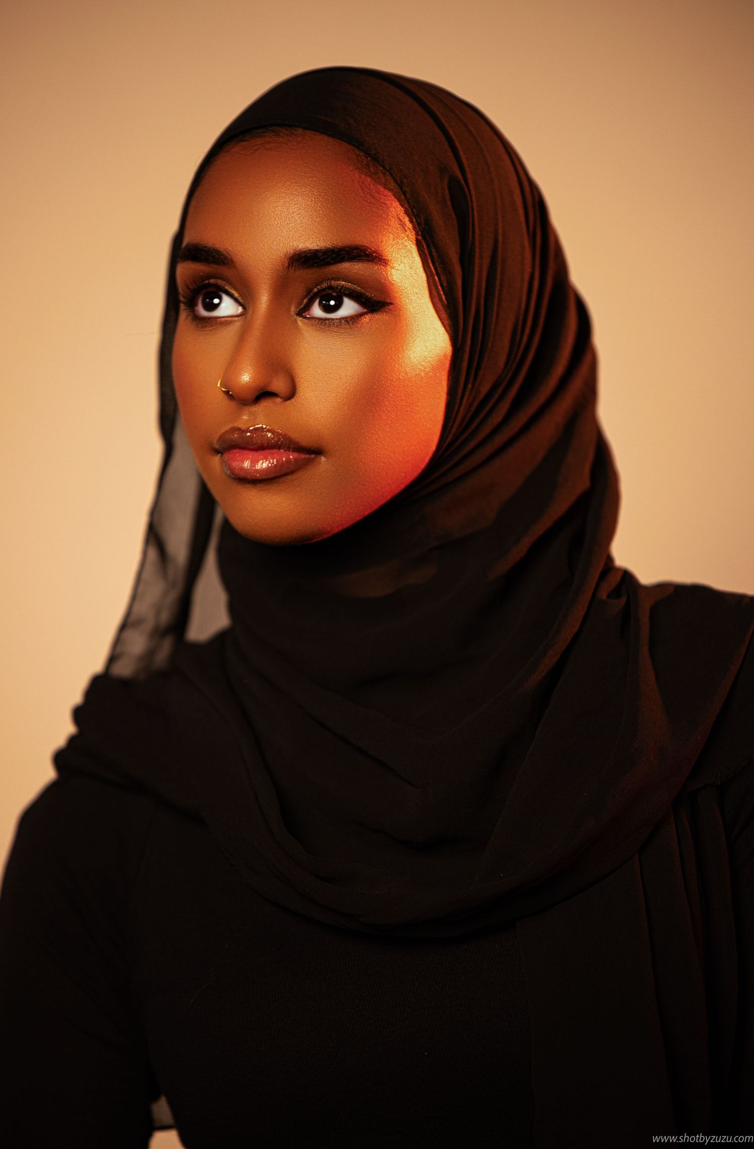 Elegant portrait featuring a woman in black hijab with dramatic lighting and makeup.
