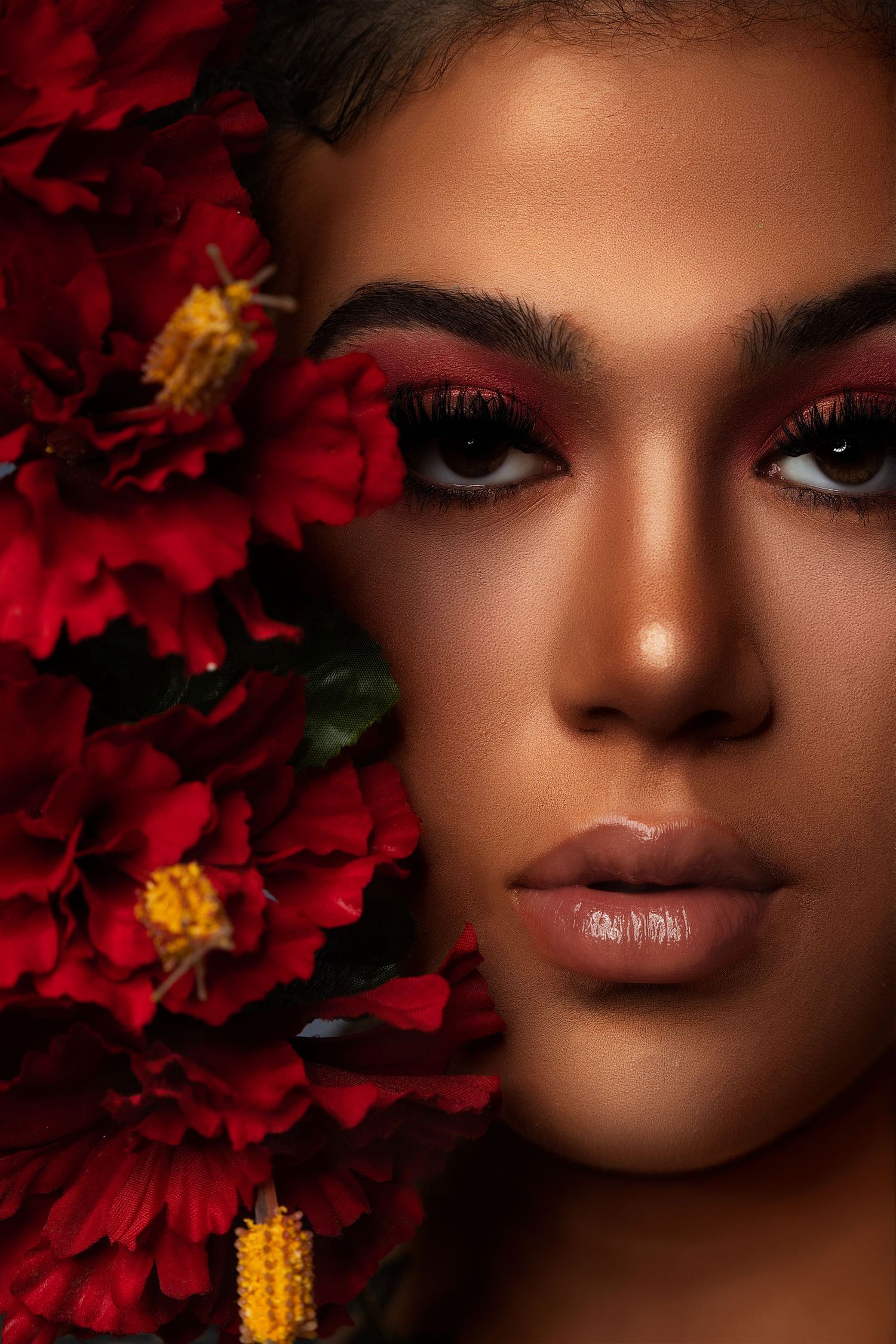 Close-up beauty portrait with vibrant red flowers and warm-toned glamour makeup.