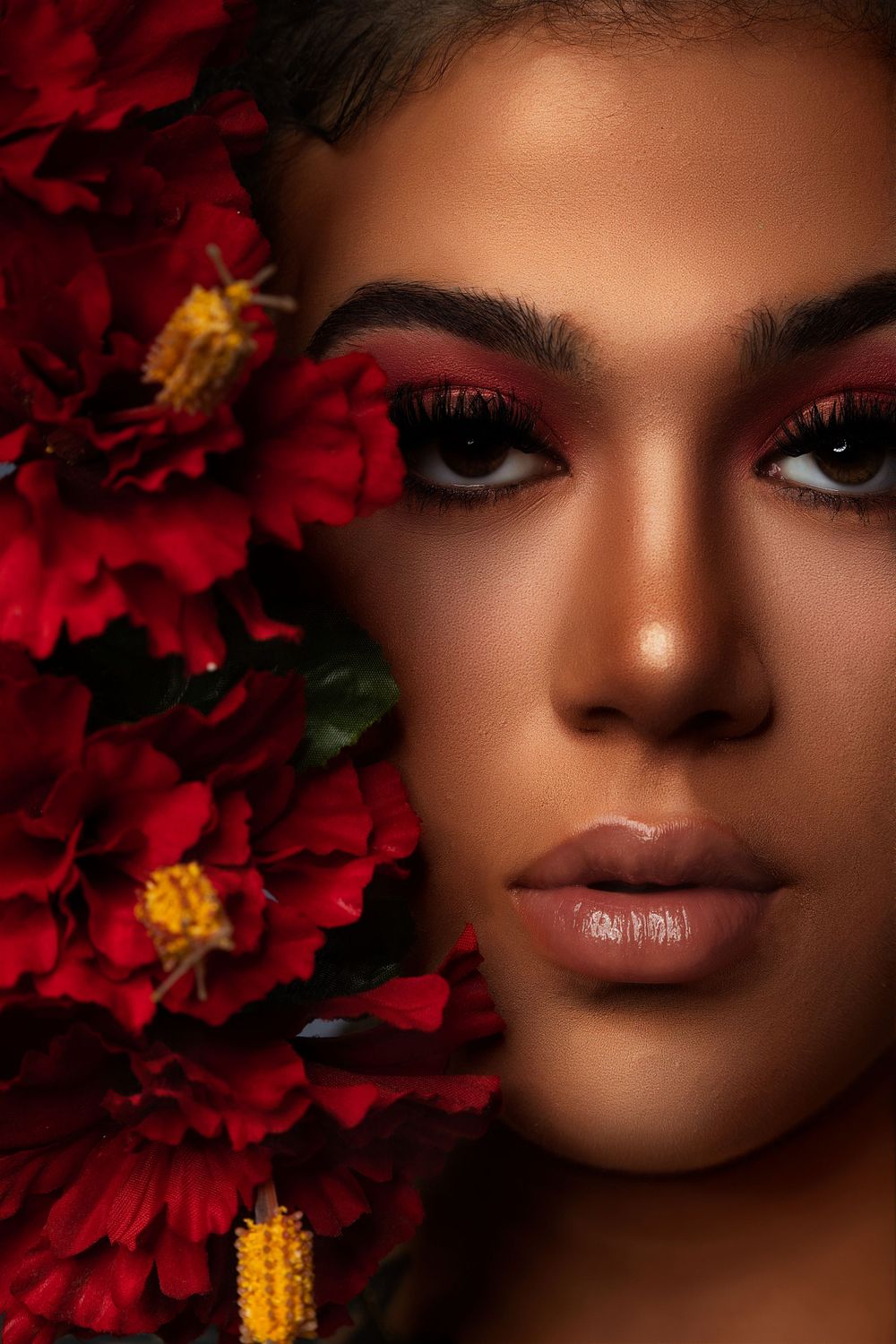 Close-up beauty portrait with vibrant red flowers and warm-toned glamour makeup.