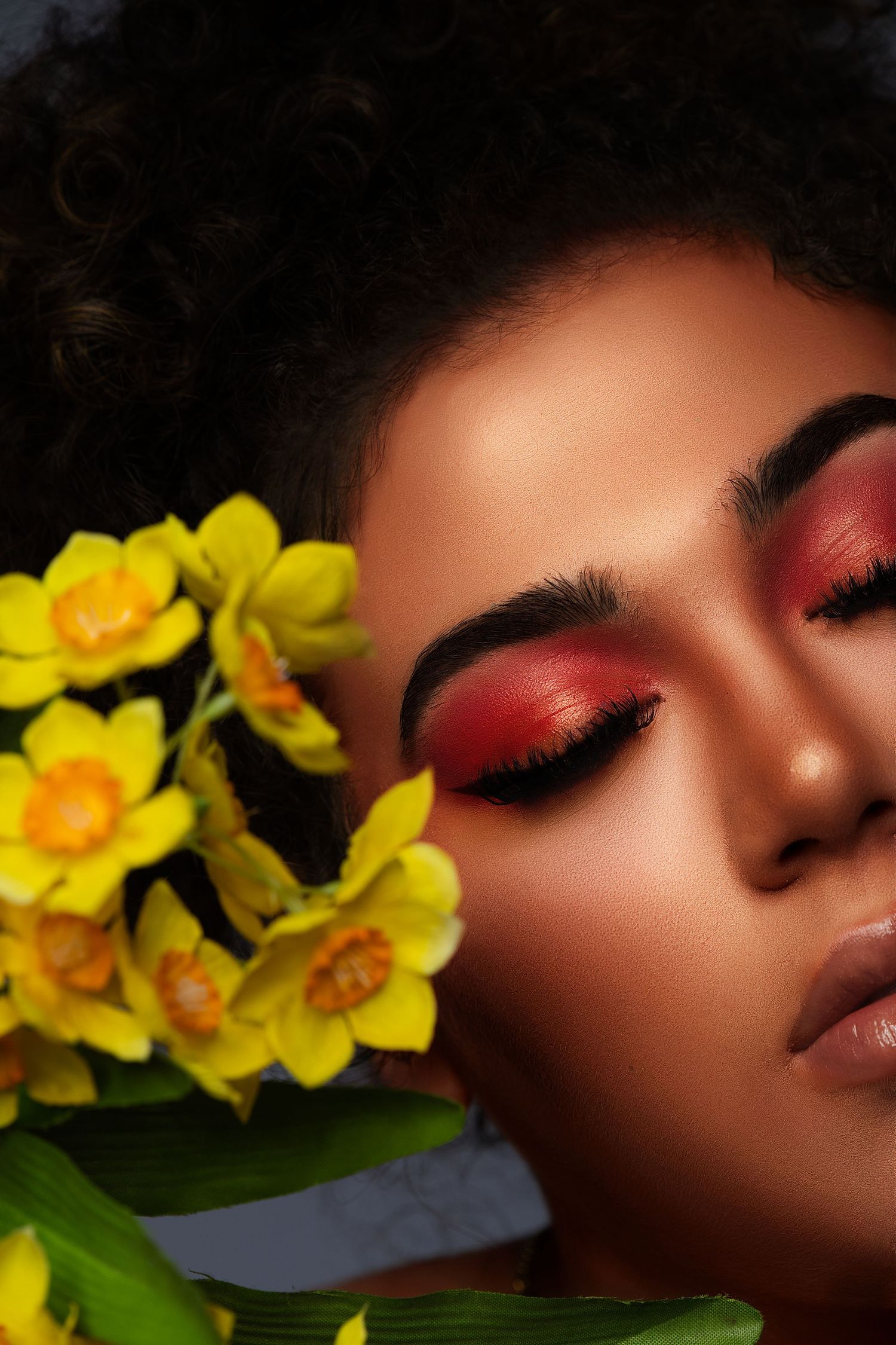 Beautiful artistic makeup look with red eyeshadow and yellow daffodils creating a spring beauty portrait.