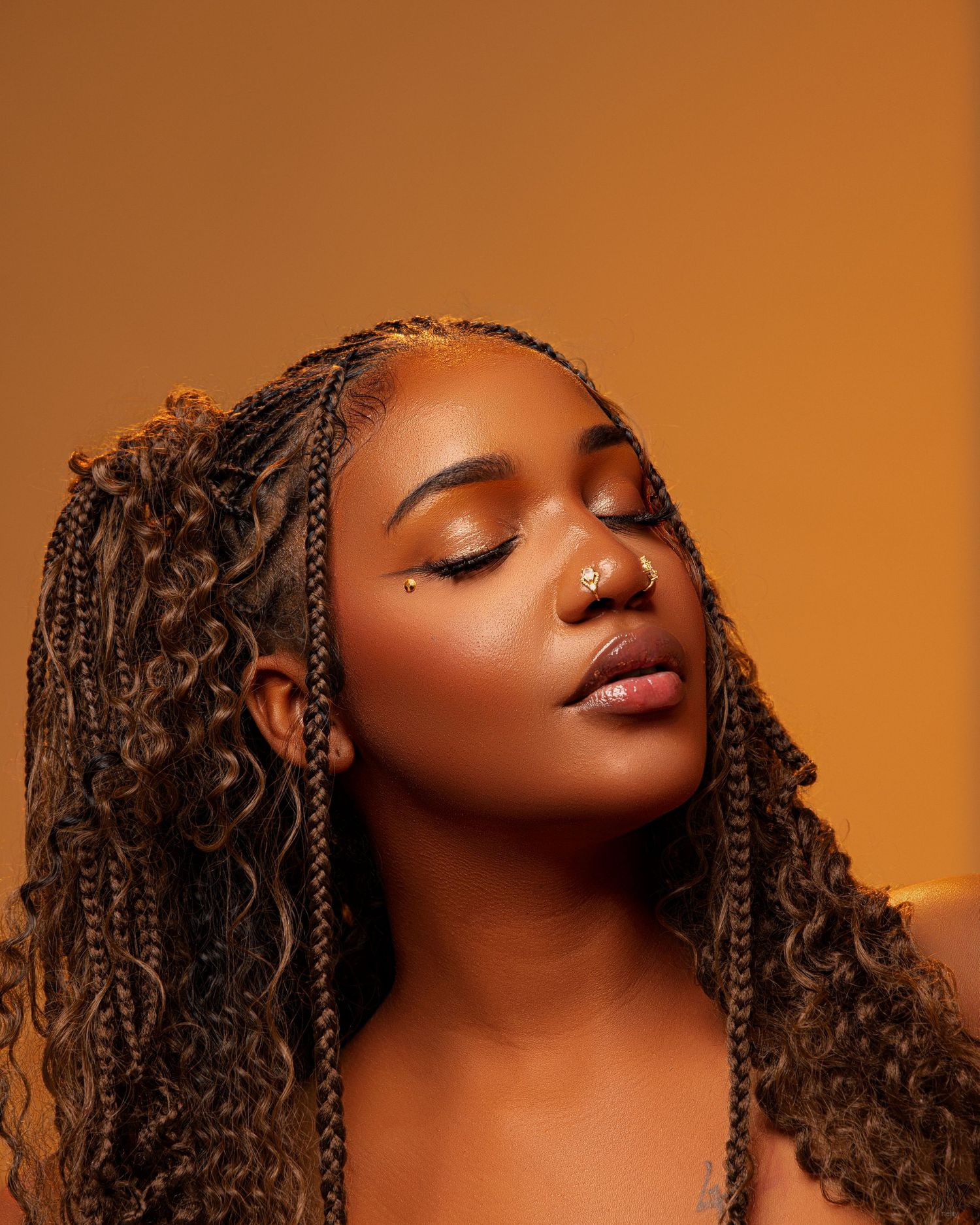 Beauty portrait with closed eyes and braided hair against orange backdrop.