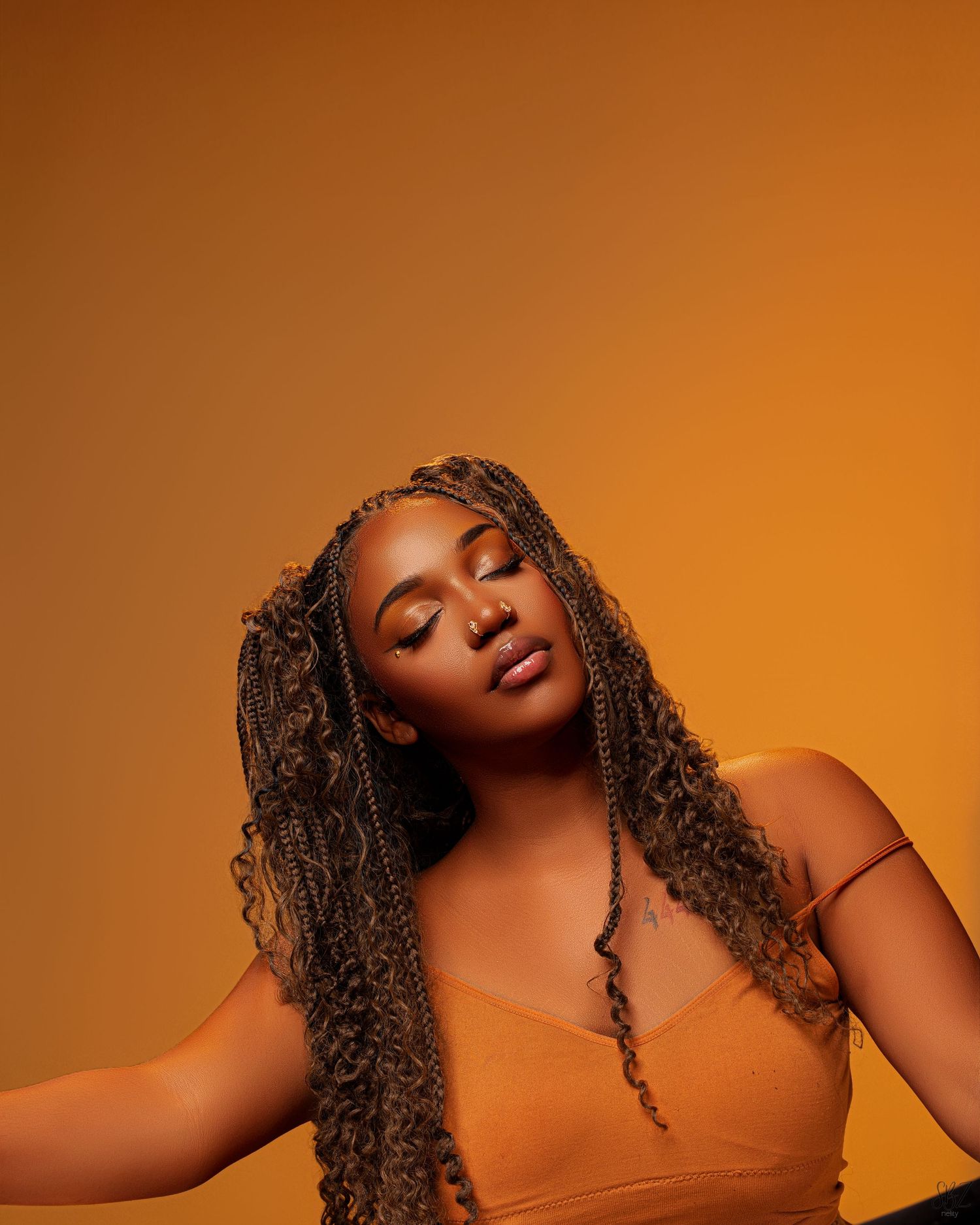 Artistic portrait of woman with braided hair in orange top against matching background.