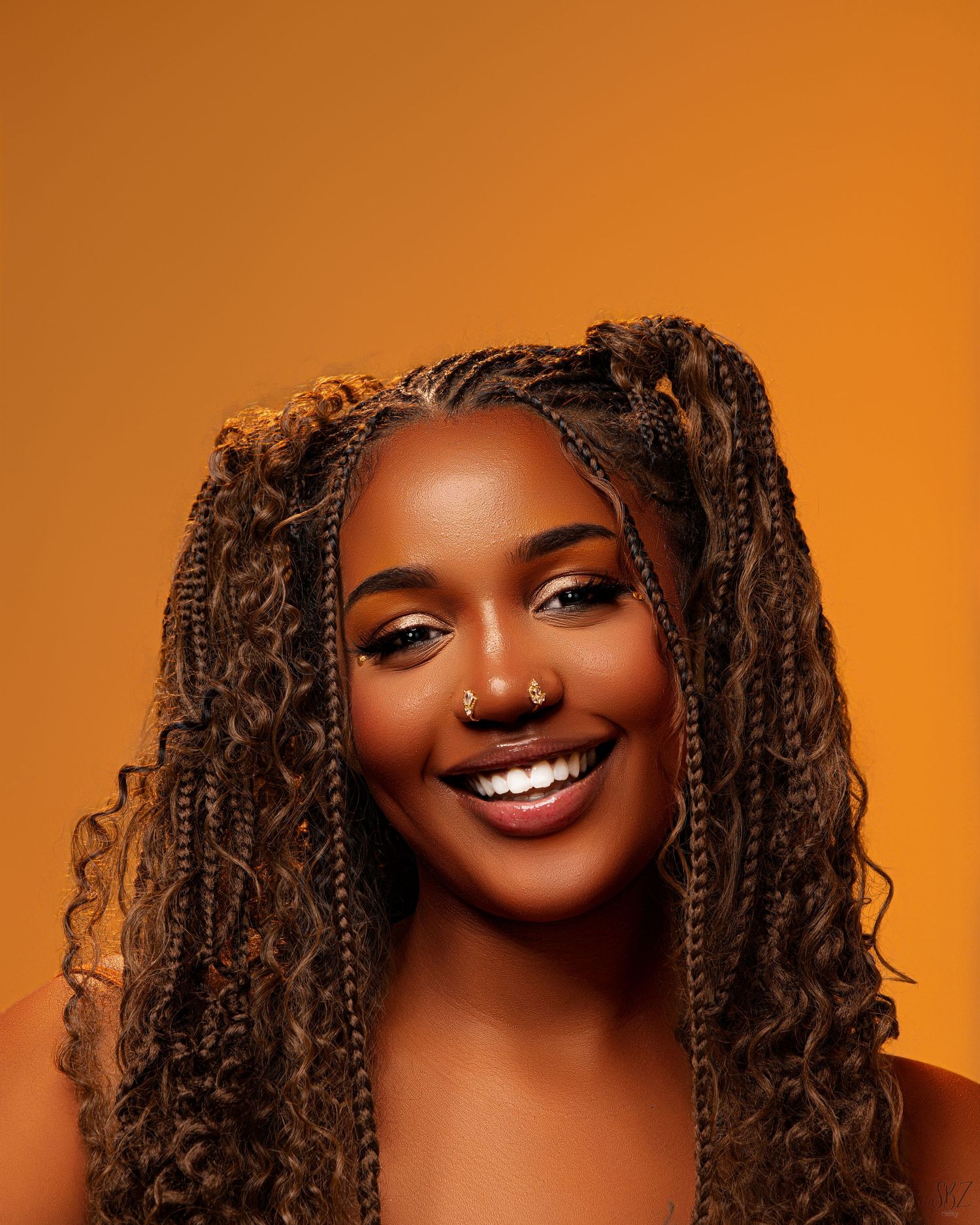 Studio portrait with curly brown braids and natural makeup against an orange background.