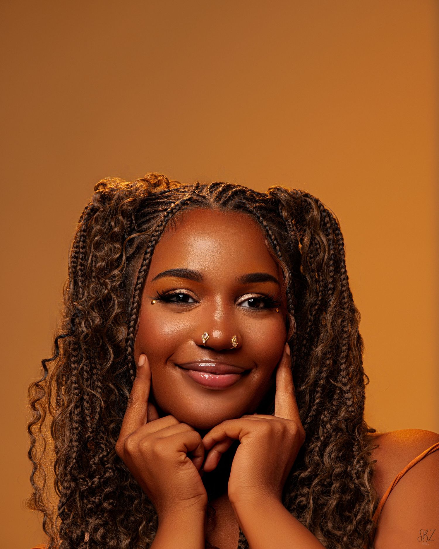 Beauty portrait featuring long braided hair and radiant smile against warm orange backdrop.