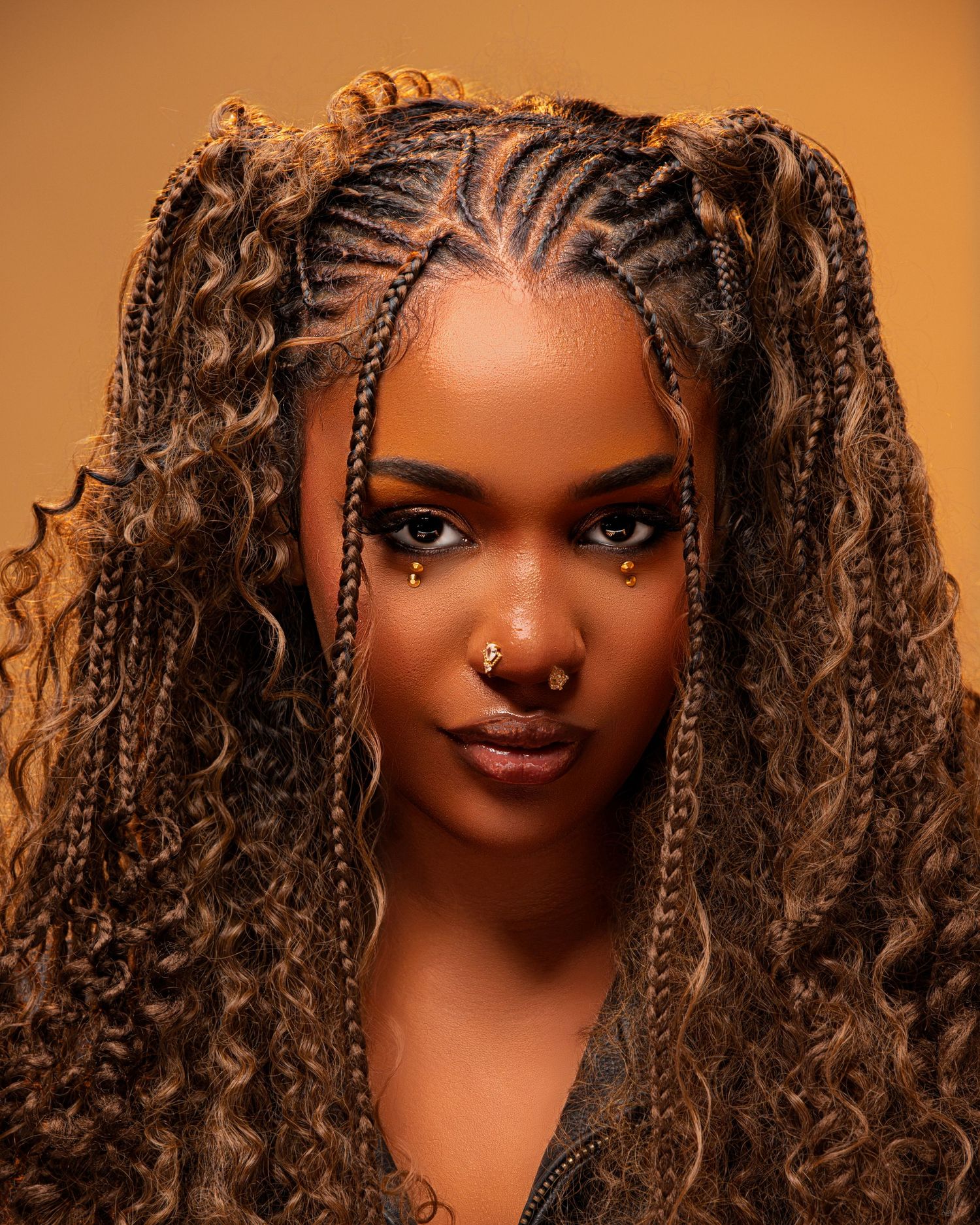 Portrait of woman with intricate braided hairstyle against warm orange background.