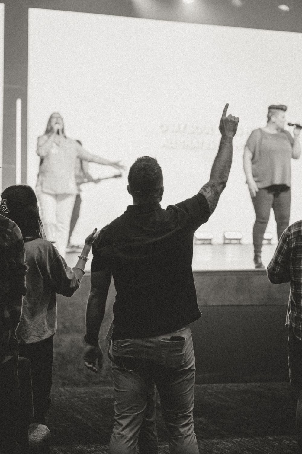 Silhouetted crowd raises their hands in worship at a church service with bright stage lights in the background.