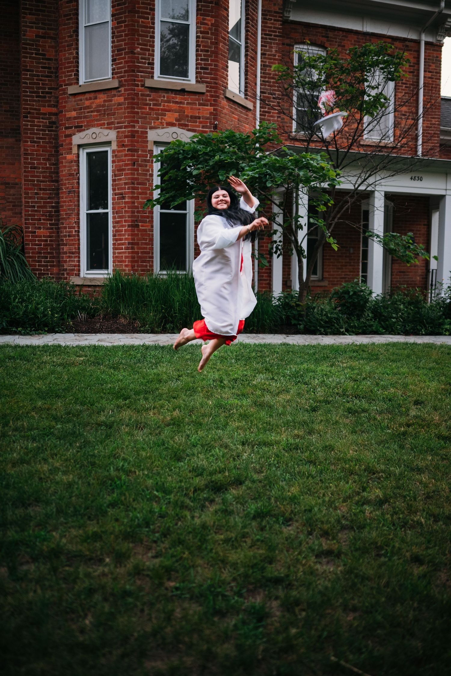 A person performs a series of dynamic jumping movements on a grassy hill in front of a brick building.