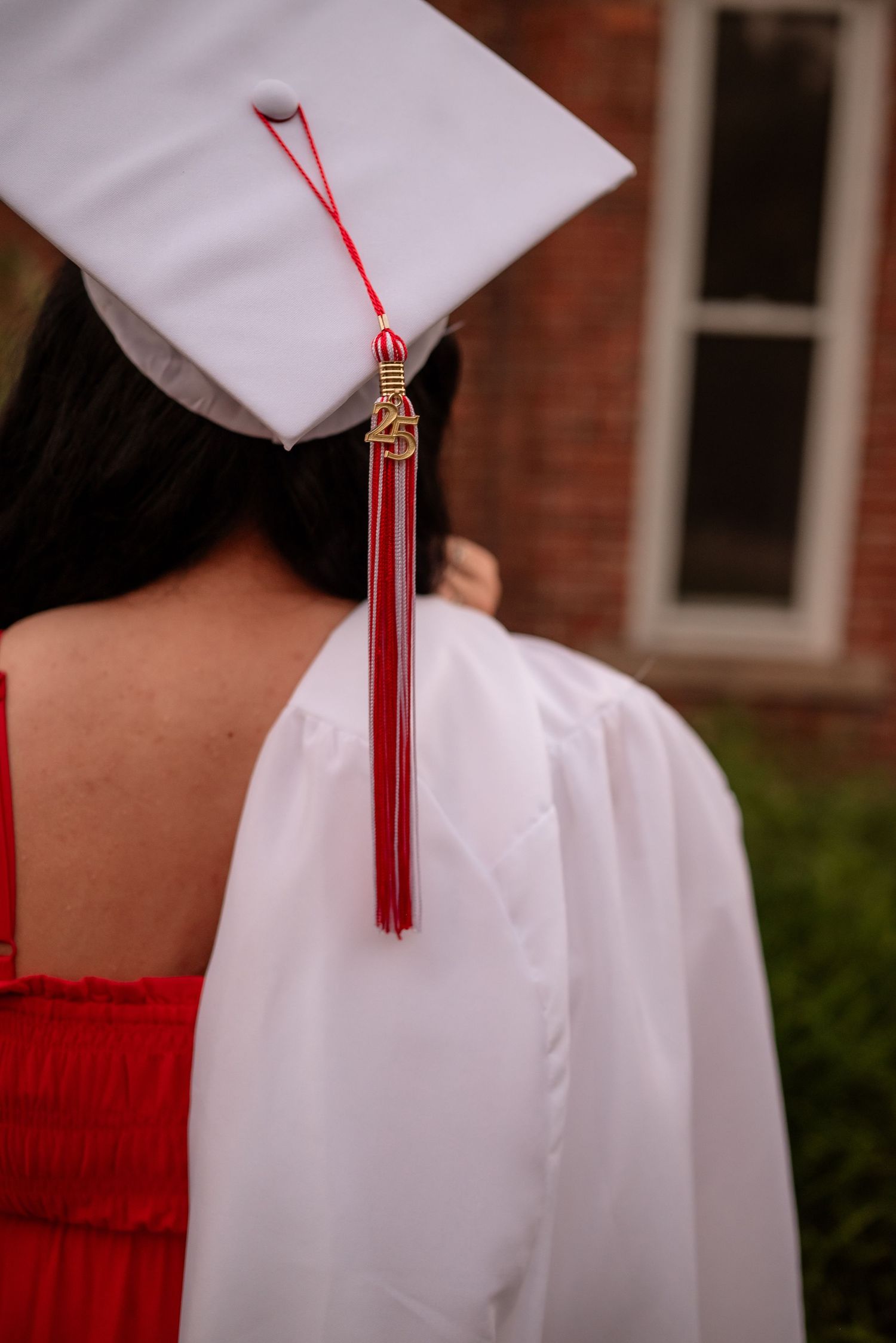 Close-up view of white graduation caps with red tassels against a brick building background.